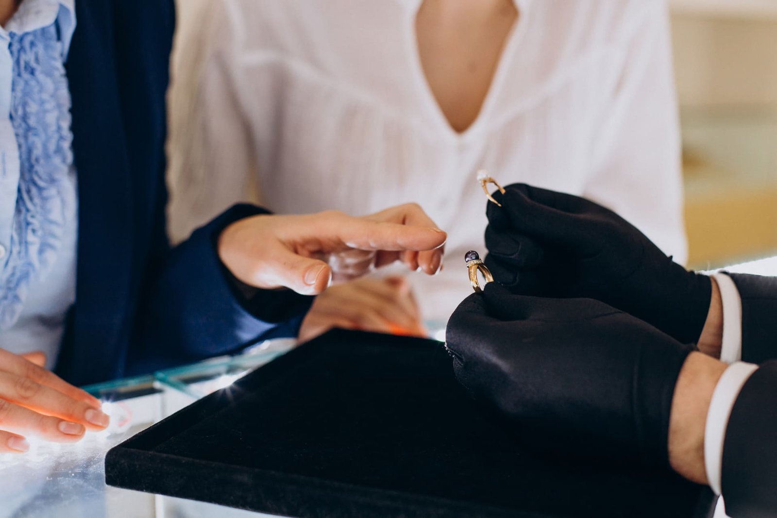 Cliente experimentando anel em uma joalheria, com atendente profissional usando luvas para demonstrar a peça.